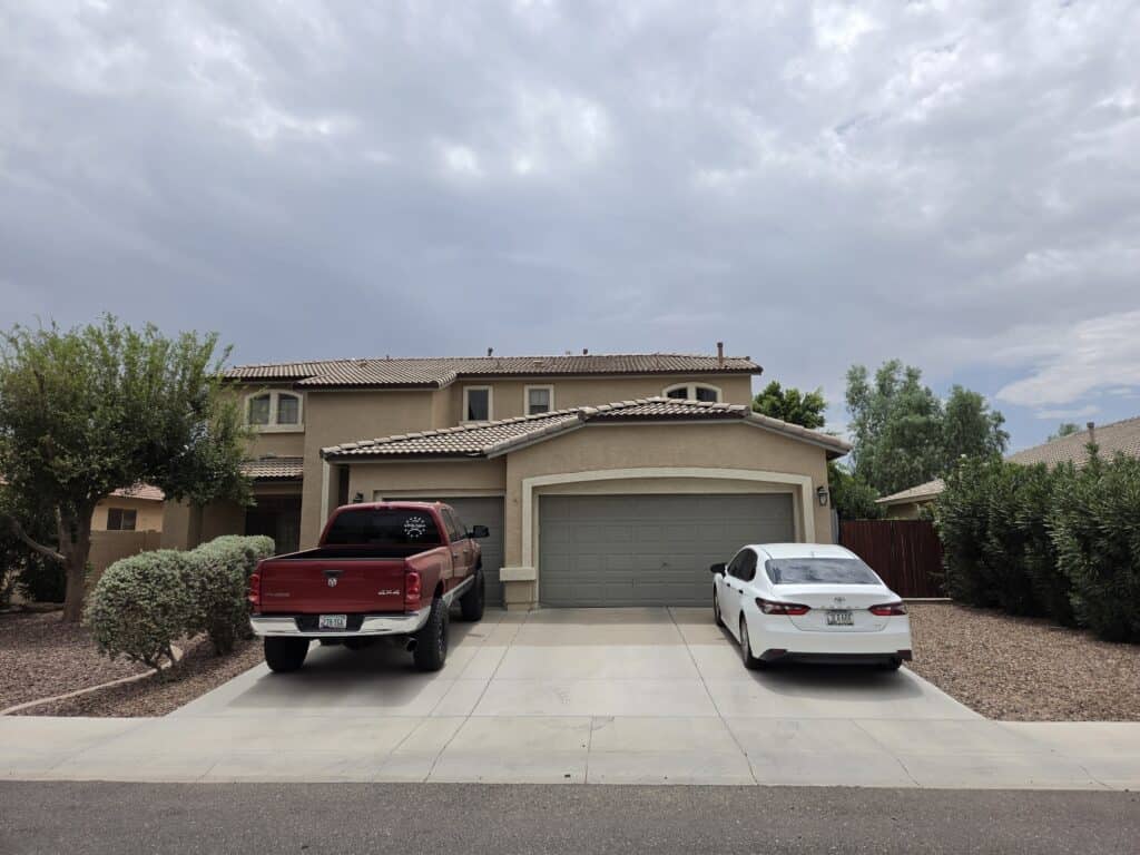 Residential house with two parked cars in driveway under cloudy sky.