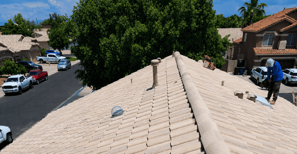 Residential roof with beige tiles and workers installing new roofing system.
