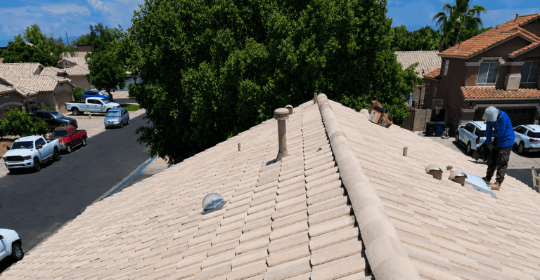 Residential roof with beige tiles and workers installing new roofing system.
